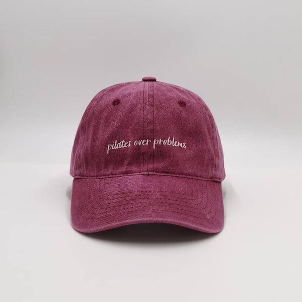 Schildmütze aus 100% Baumwolle in Rot mit eingesticktem Spruch. Der Spruch lautet: pilates over problems