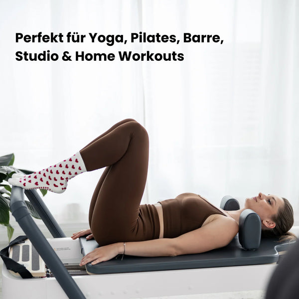 Beige Pilates Grip Socks mit rutschfester Sohle aus bordeauxfarbenen Herz-Noppen, getragen auf einem Reformer beim Training. Ideal für Reformer Pilates, Yoga und Barre.