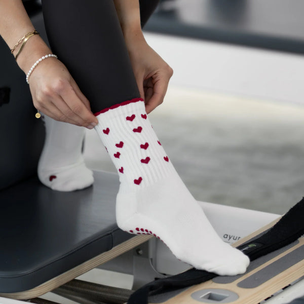 Beige Pilates Grip Socks mit bordeauxroten Herzmustern und rutschfestem Profil, getragen auf einem Reformer. Ideal für Pilates, Yoga und Barre.