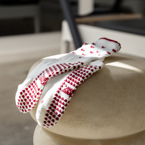 Beige Pilates Grip Socks mit bordeauxfarbenen Herz-Noppen und Herzmuster, flach drapiert im Tageslicht. Rutschfestes Design für Pilates, Yoga, Barre und Freizeit.