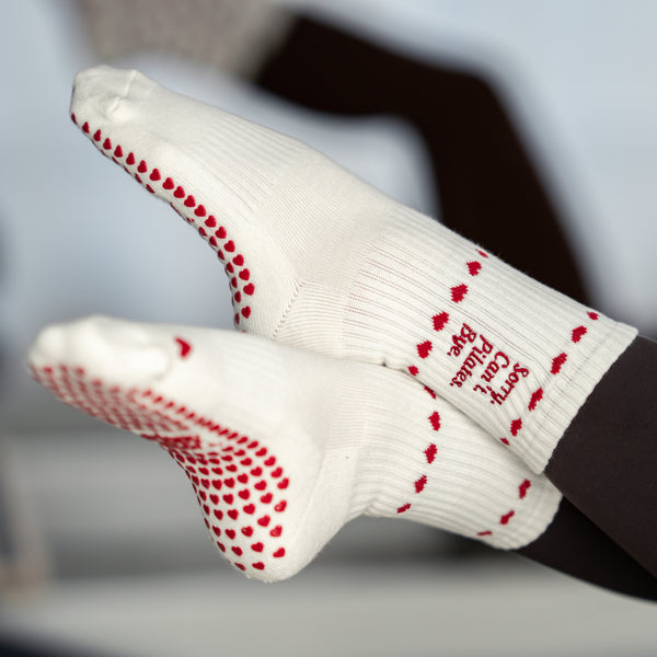 Close-Up der Sohle: beigefarbene Pilates Socken mit roten Herz-Noppen und Statement-Schriftzug – stylisch, rutschfest und studio-ready