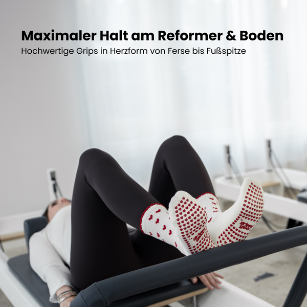 Beige Pilates Grip Socks mit rutschfester Sohle aus bordeauxfarbenen Herz-Noppen, getragen auf einem Reformer beim Training. Ideal für Reformer Pilates, Yoga und Barre.