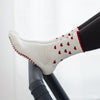 Beige Pilates Grip Socks mit rutschfester Sohle aus bordeauxfarbenen Herz-Noppen, getragen auf einem Reformer beim Training. Ideal für Reformer Pilates, Yoga und Barre.
